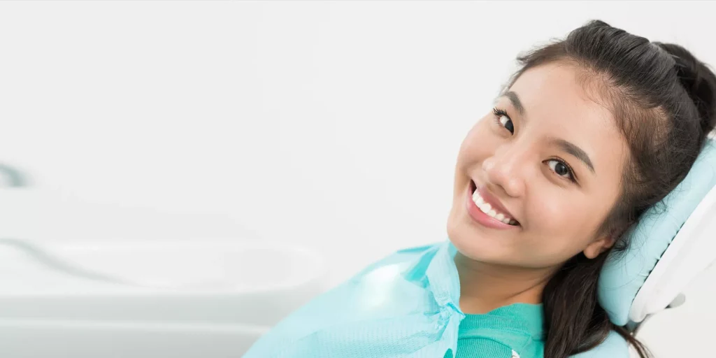 A woman smiles while sitting in a dental chair, experiencing sedation dentistry.